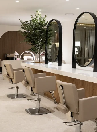 Modern hair styling stations featuring a long white counter, tall black oval mirrors, and beige salon chairs at Unique Beauty & Style in Perth.